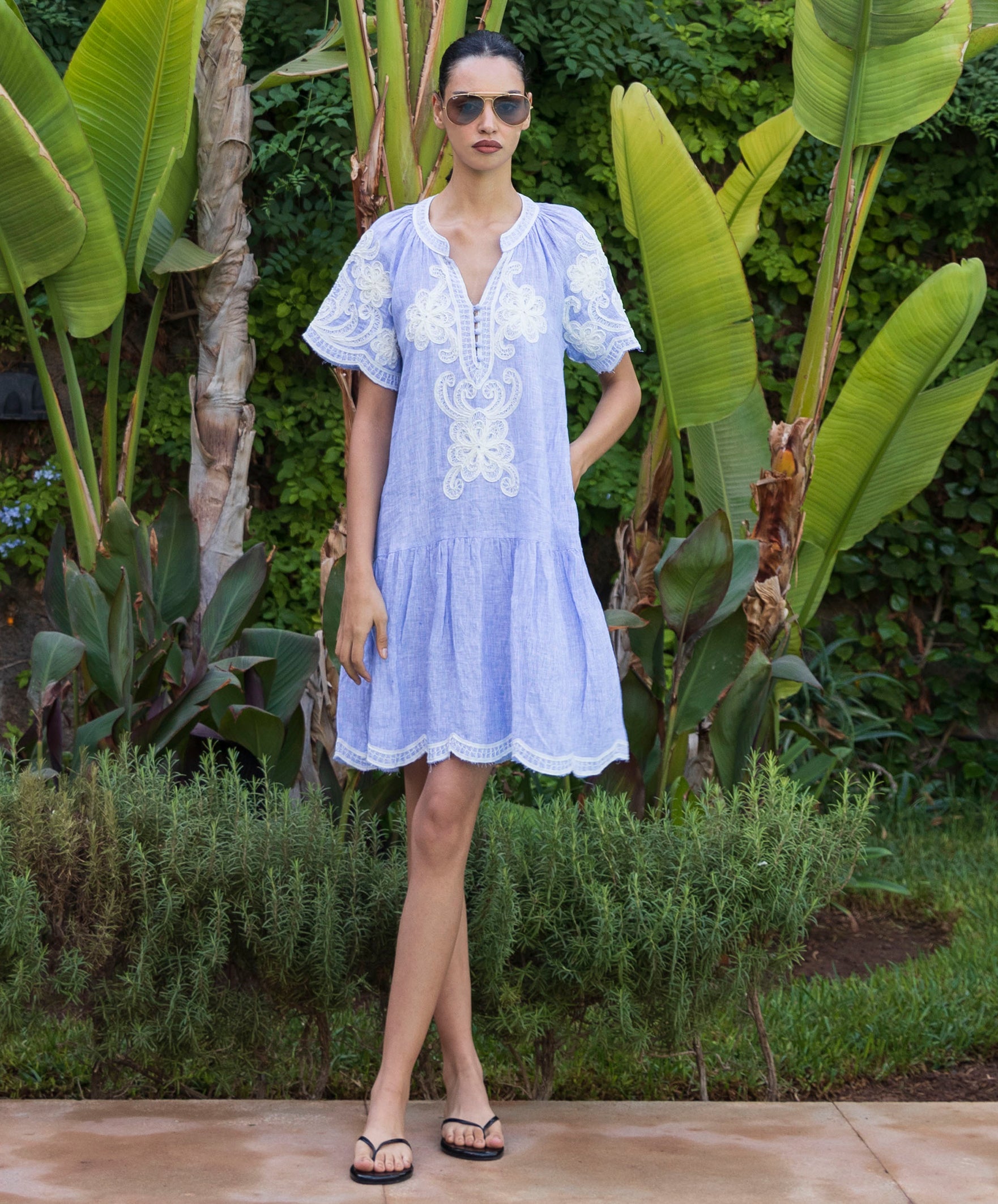 Woman in a blue striped Amaranta dress with tapework decoration standing in a tropical garden.