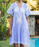 Striped blue Amaranta dress with white floral tapework decoration worn by a pool.