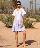 Woman in a striped blue Amaranta dress with white tape decoration standing in a desert-like setting.