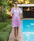 Woman in a red striped Amaranta dress with tape work decoration standing by a pool.