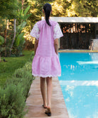 Back view of a woman in a red striped Amaranta dress with tape work decoration walking by a pool.