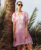 Woman in a red striped Amaranta dress with white tape decoration leaning on a palm trees