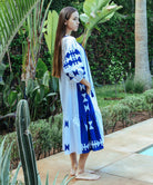 Side view of a model wearing a Rose and Rose Amersham cotton dress in white with cobalt appliqué decoration. 