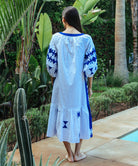 Back view of a model wearing a Rose and Rose Amersham cotton dress in white with cobalt appliqué decoration. 