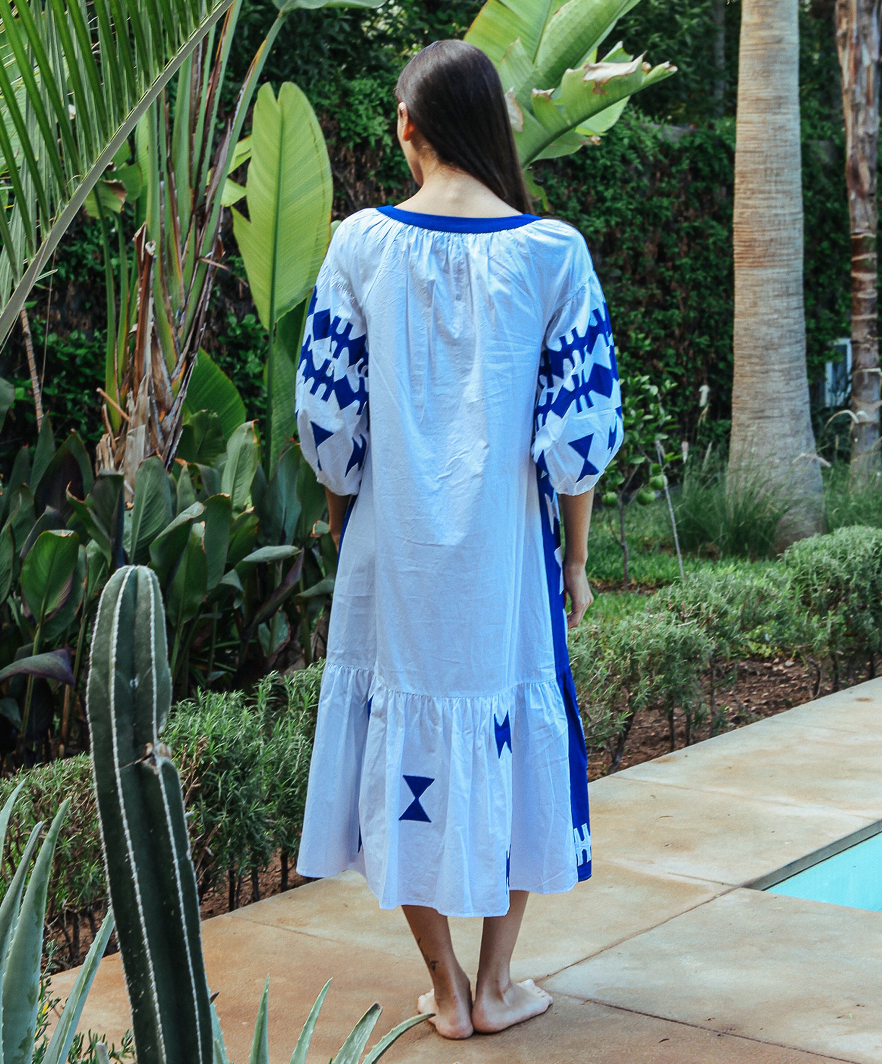 Back view of a model wearing a Rose and Rose Amersham cotton dress in white with cobalt appliqué decoration. 