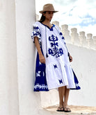 A model wearing a Rose and Rose Amersham cotton dress in white with cobalt appliqué decoration. 