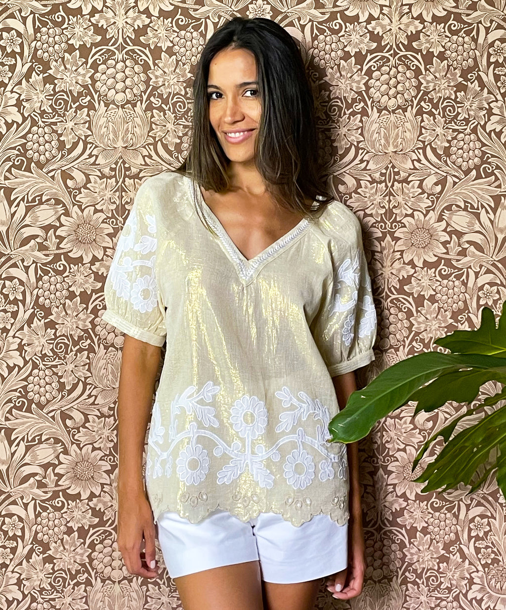 A model stood in front of floral wallpaper wearing the Rose and Rose gold lurex Anacapri top with white applique. 