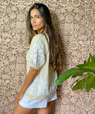 A model stood in front of floral wallpaper wearing the Rose and Rose gold lurex Anacapri top with white applique. 