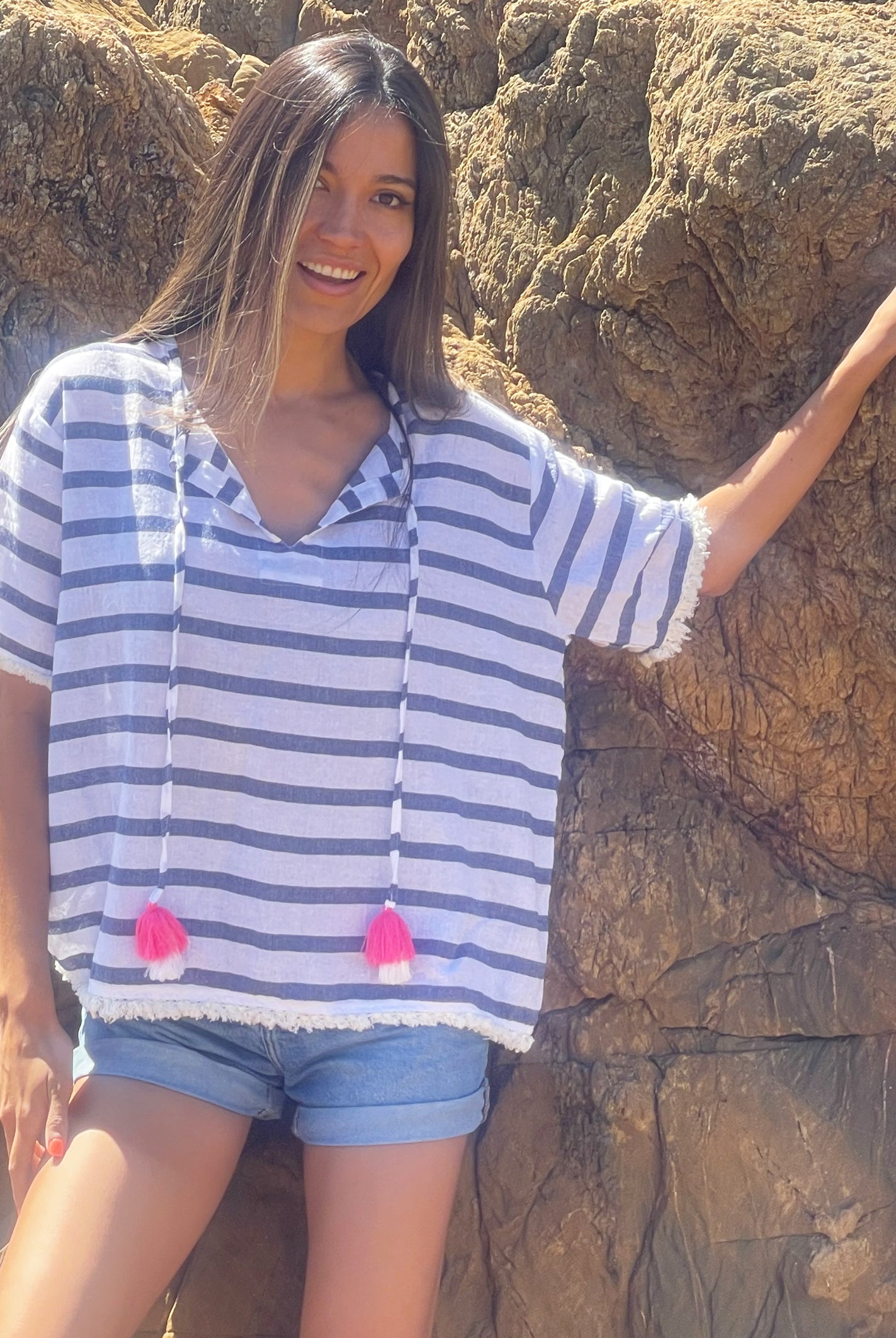 A close up of a model in front of rocks wearing a Rosebud by Rose and Rose Antibes top and denim cut off shorts. 