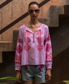 Woman wearing a pink floral embroidered Ash top and denim shorts, standing against a textured wall.