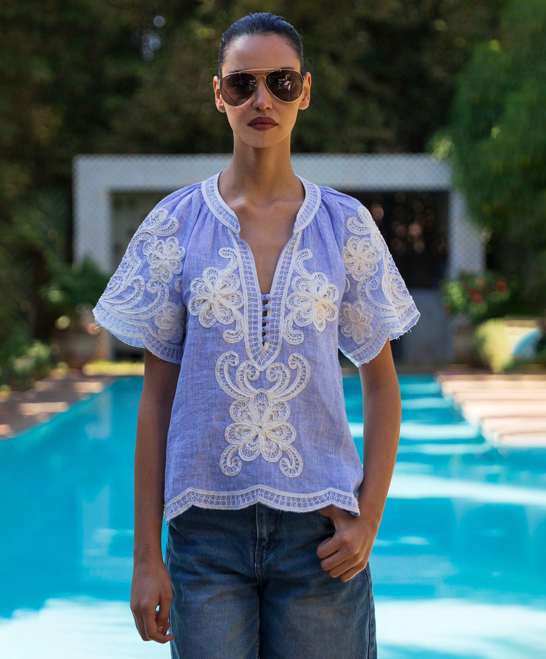 Woman wearing a blue striped embroidered Azalea top by a pool
