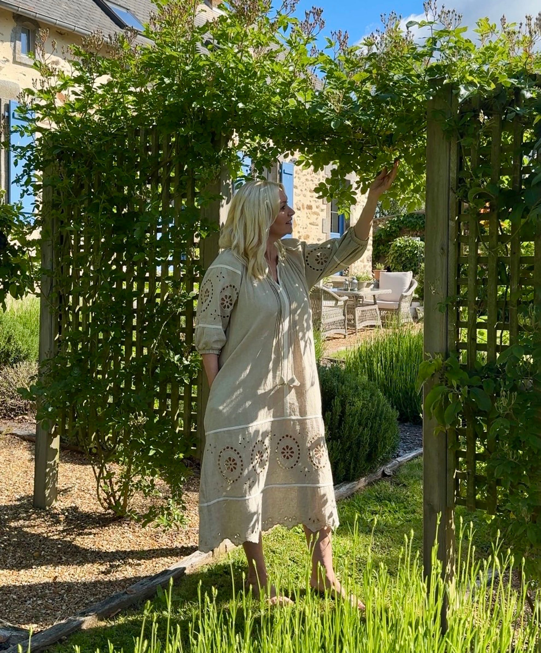 Influencer @shutters_and_stone stood admiring her garden wearing the Magnolia natural embroidered dress 
