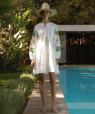 Woman in a Beech white dress with colorful sequined sleeves standing by a pool