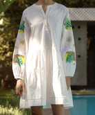 Beech white dress with colorful floral sequins on sleeves, worn in garden.