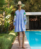 Woman in a light blue Beech dress with sequin decorated sleeves standing by a poolside.