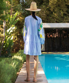 Back view of a woman wearing a light blue dress with sequin decoration, standing by a pool.