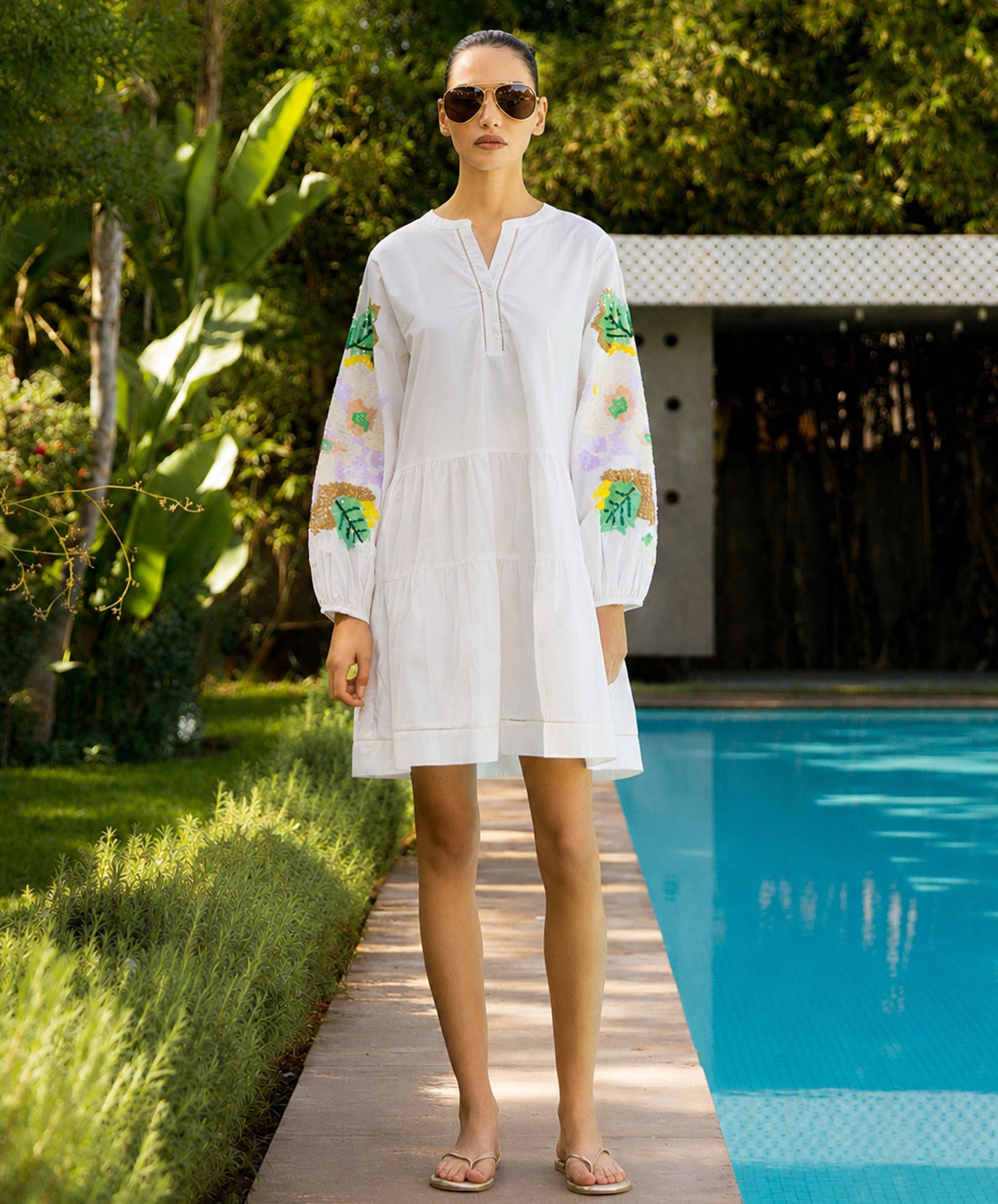 Woman in a white dress with colorful sequins on the sleeves standing by a pool