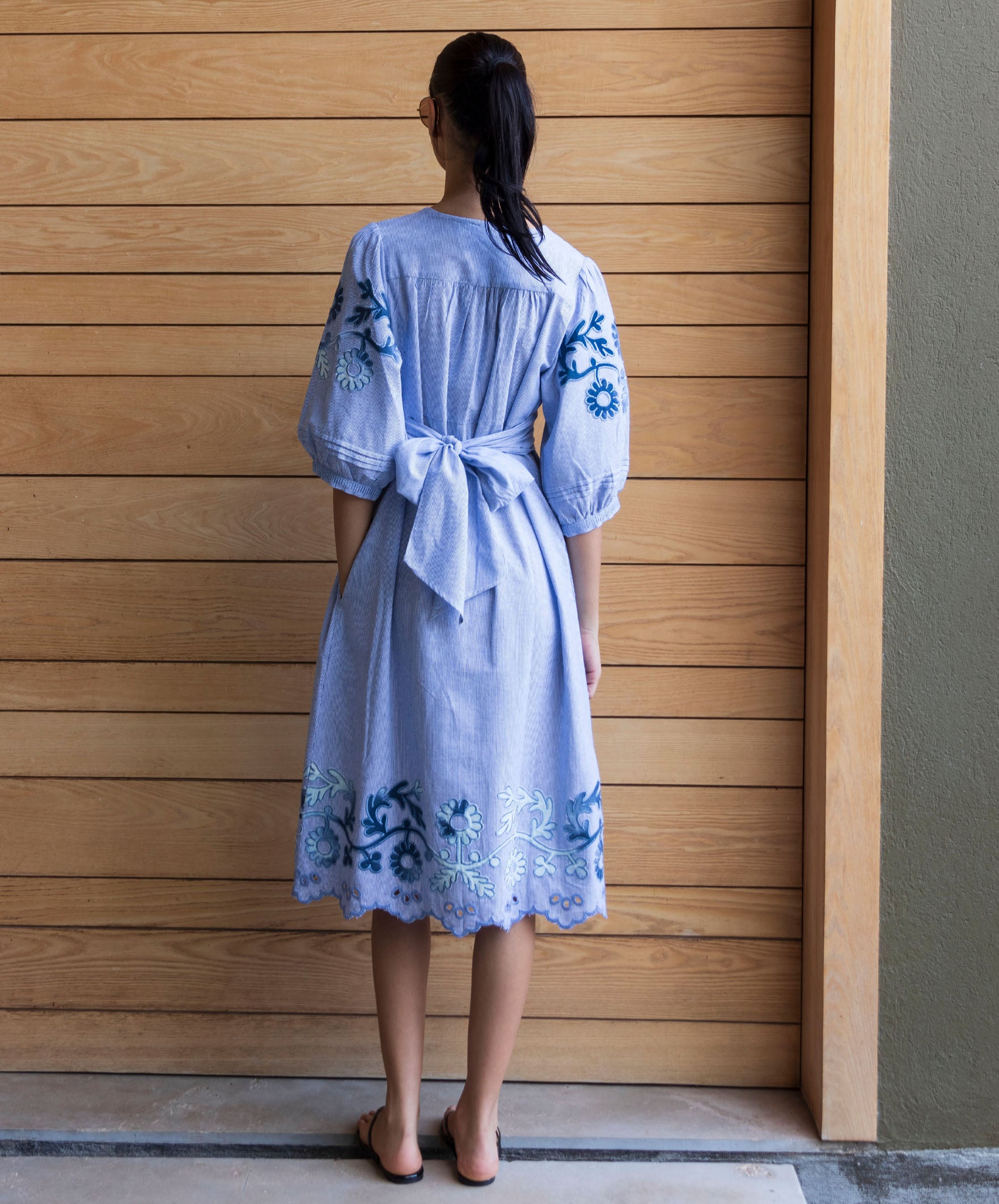 Back view of a woman wearing a blue striped Begonia dress with denim applique decoration.