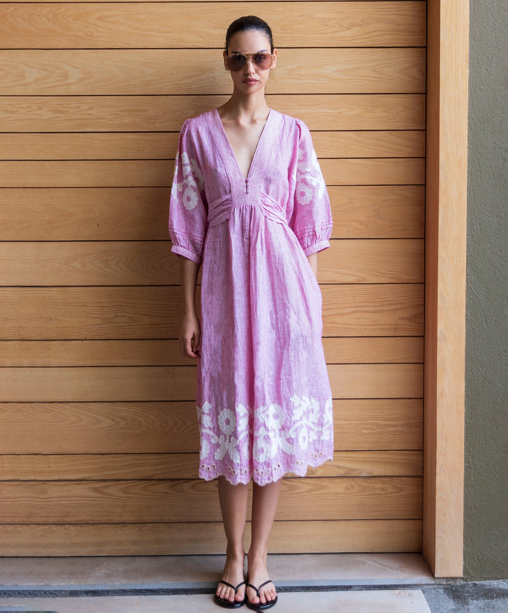 Woman wearing a red striped Begonia dress with floral applique decoration against a wooden wall.