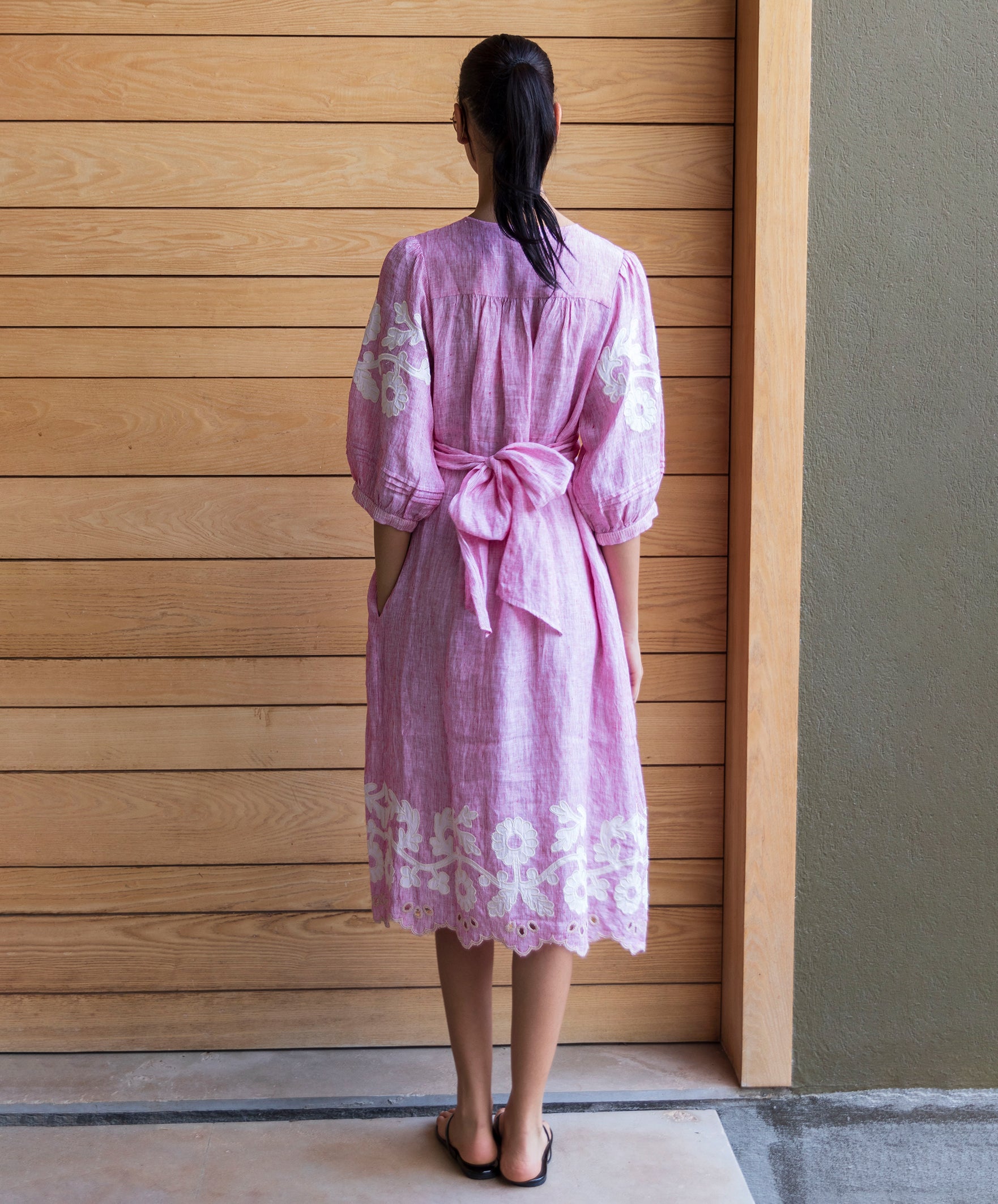 Back view of a woman wearing a red striped Begonia dress with floral applique decoration standing against a wooden door.