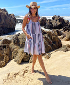 A model stood on a beach with her hands in her pockets wearing a Rosebud by Rose and Rose Biarritz dress and straw hat. 