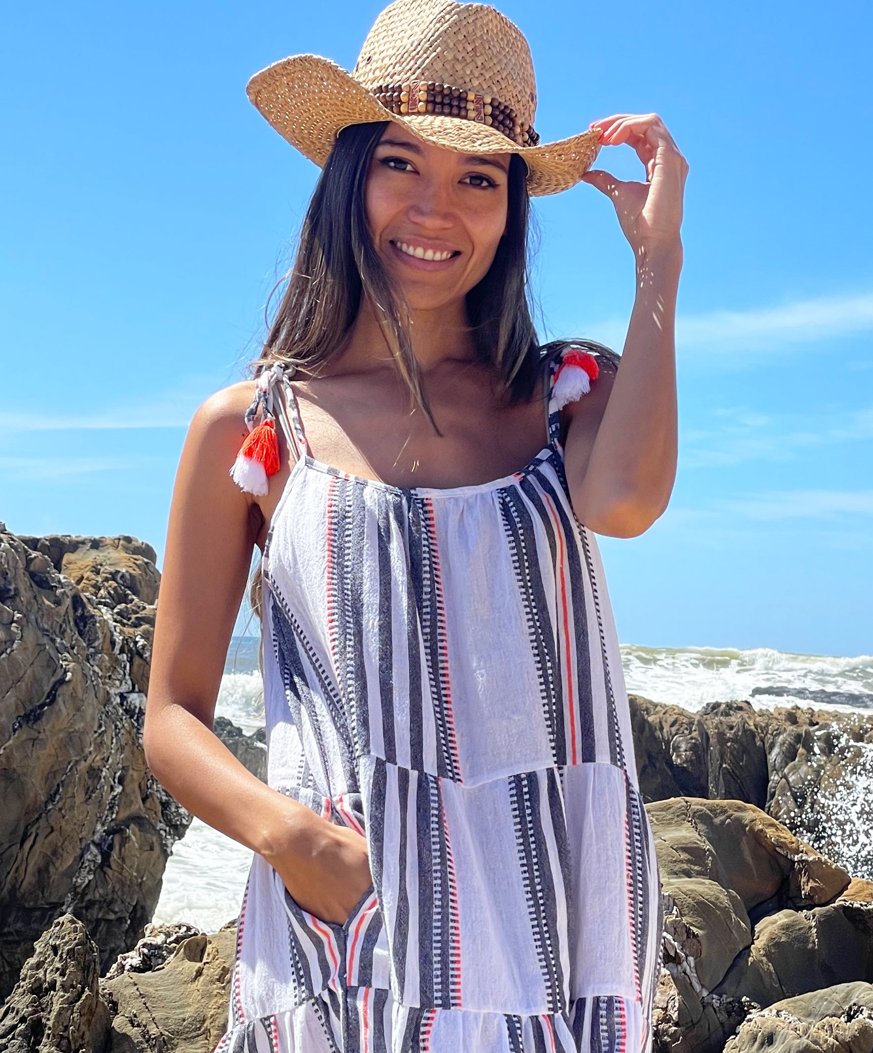 A close up of model stood on a beach wearing a Rosebud by Rose and Rose Bias Dress and straw hat.