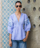 Woman wearing a blue striped Blossom  embroidered blouse and sunglasses against a textured wall.