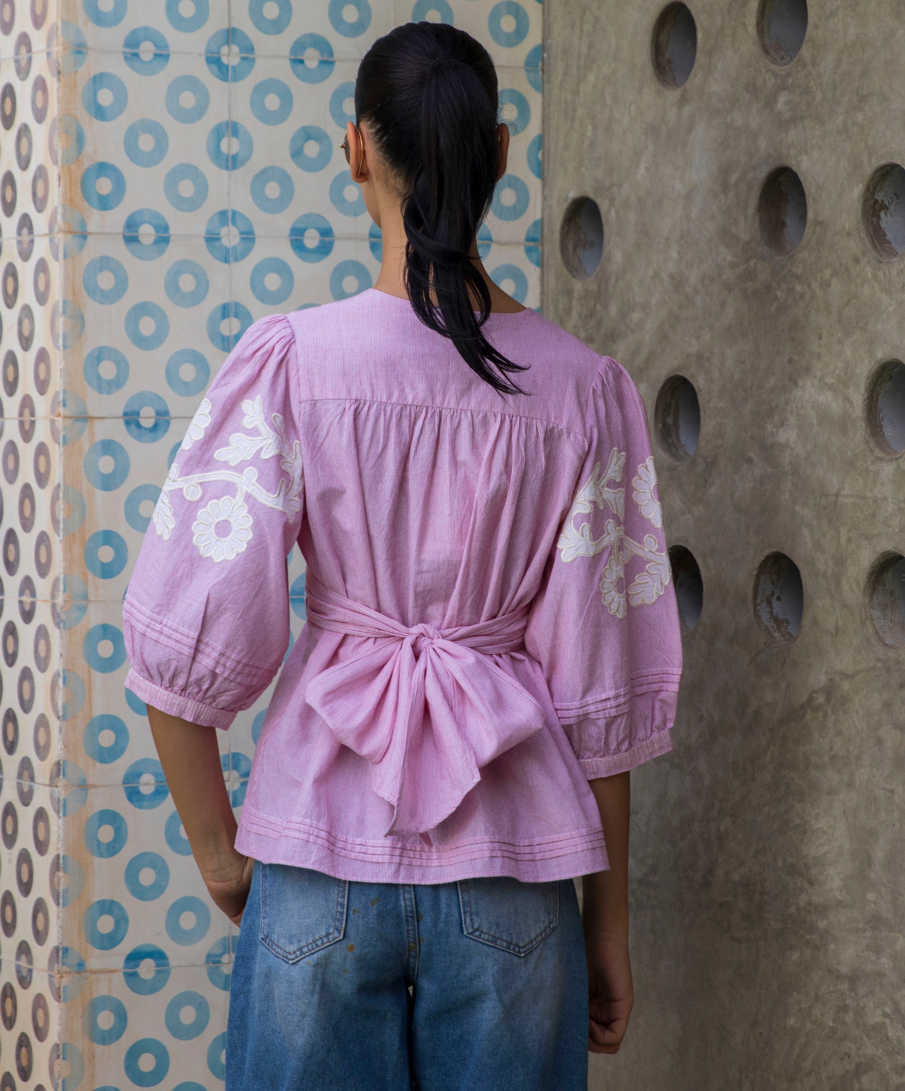 Woman wearing a red striped Blossom blouse with floral patterns and blue jeans against a patterned wall.