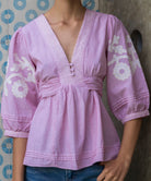 Red striped Blossom  blouse with white floral embroidery on a patterned wall background