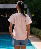 Back view of a women wearing a light pink Clematis top and shorts by a poolside