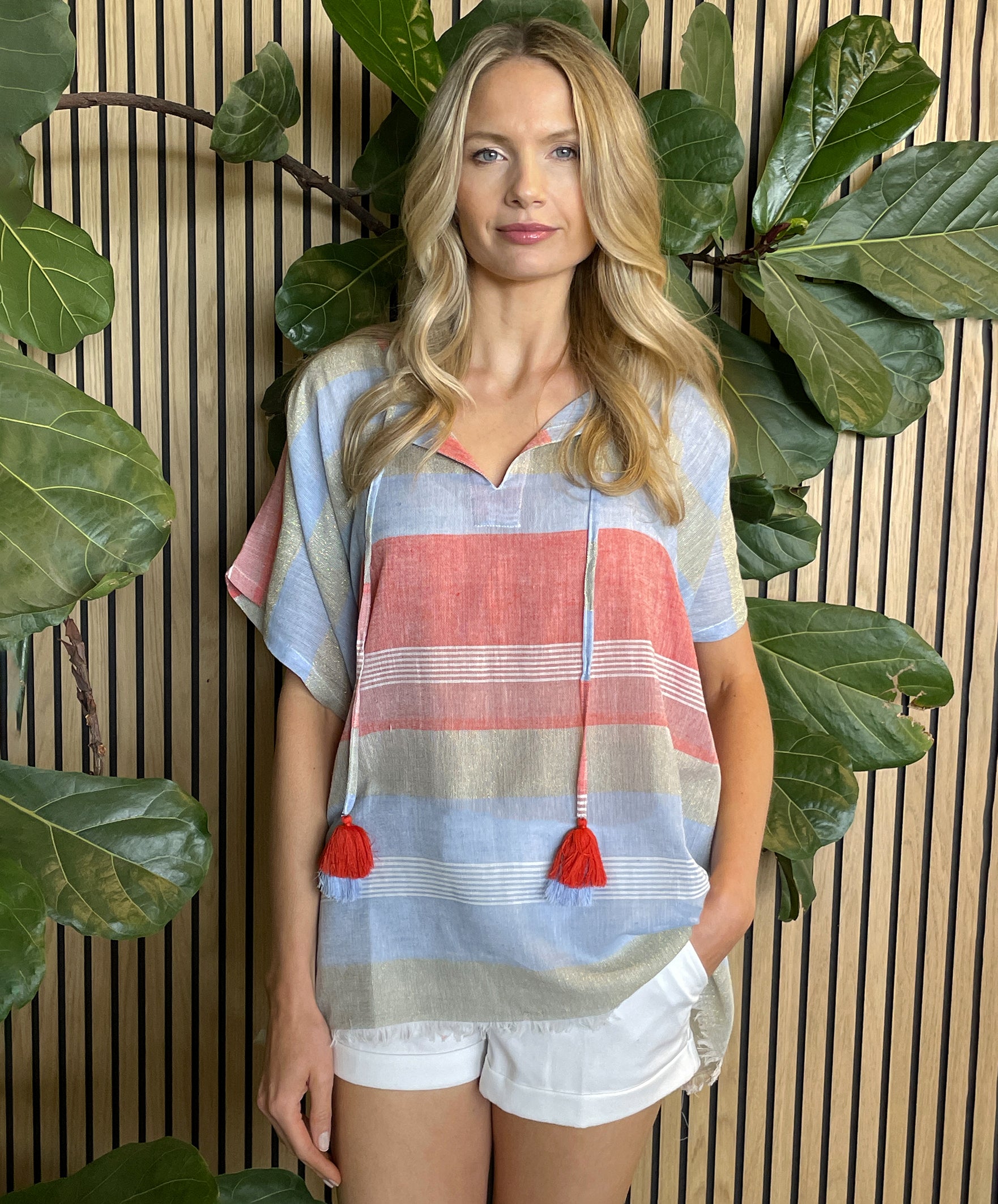 A model wearing a Rosebud by Rose and Rose red, blue and gold striped kaftan top with white shorts