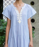 Striped blue Camelia dress with white passementerie embroidery details worn by a woman