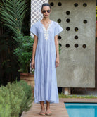 Woman in a striped blue Camelia dress  with passementerie embroidery standing by a pool