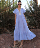Woman in a striped blue Camelia dress standing in a desert-like setting with palm trees.