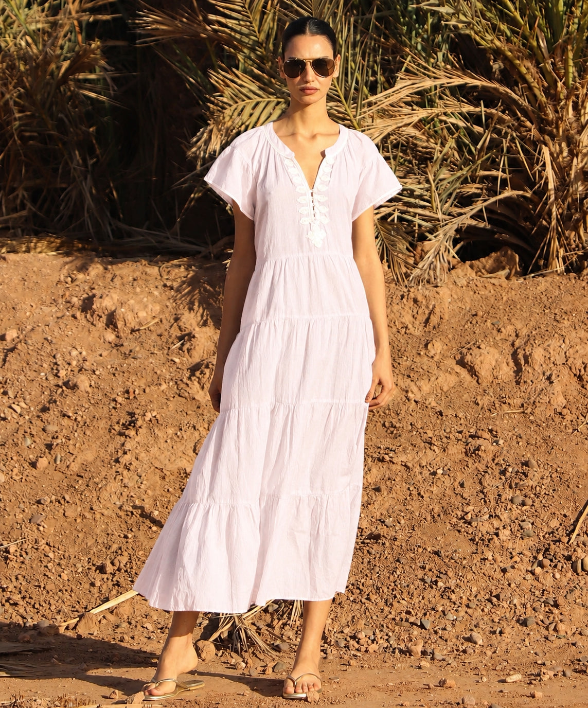 Woman in a pale pink dress standing in a desert-like setting with palm trees.