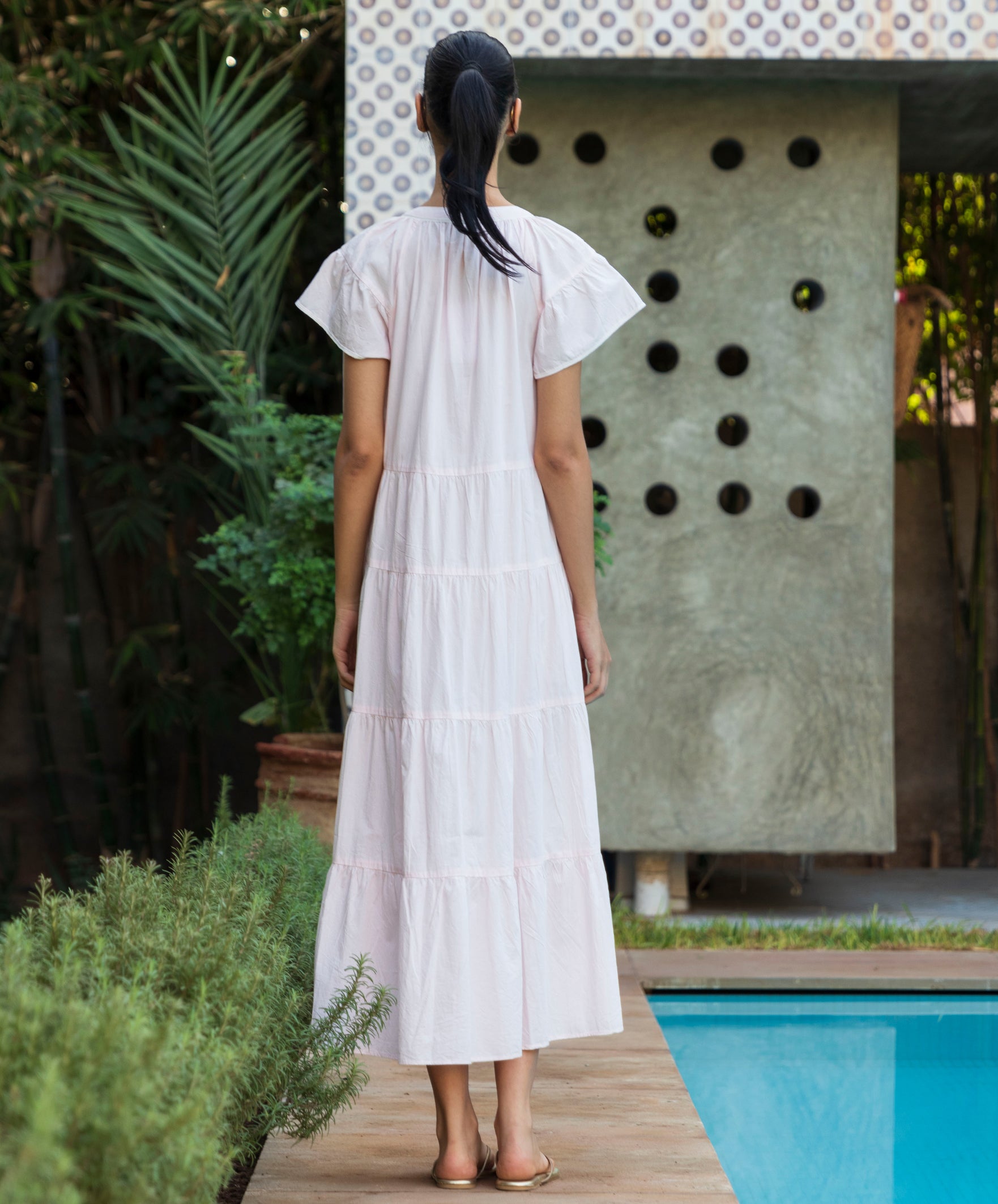 Back view of a woman in a light pink Camelia dress standing by a pool