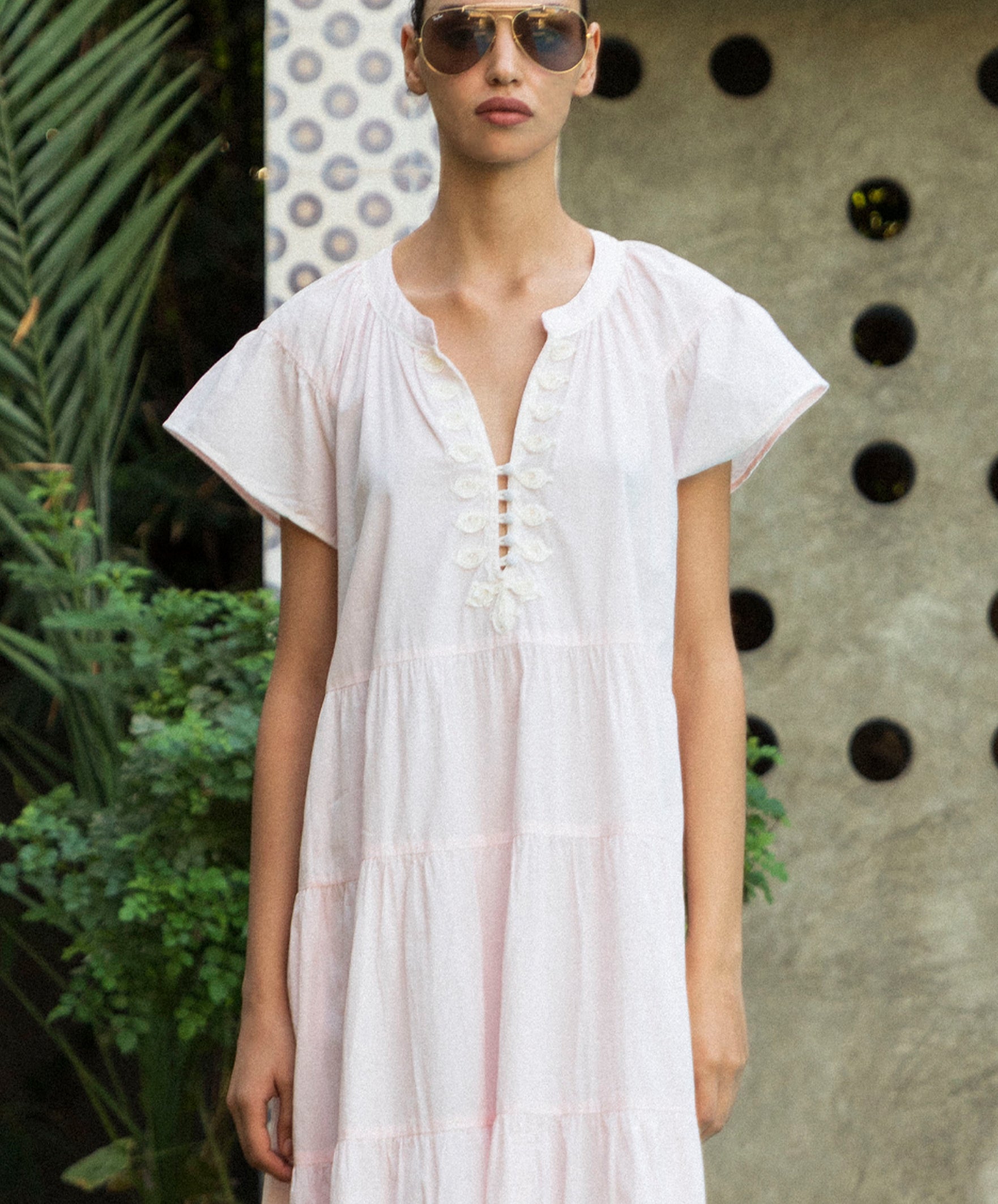 Close up of a woman wearing a light pink Camelia dress with passementerie embroidery in white. 