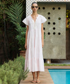 Woman in a light pink Camelia dress with white passementerie embroidery standing by a pool 