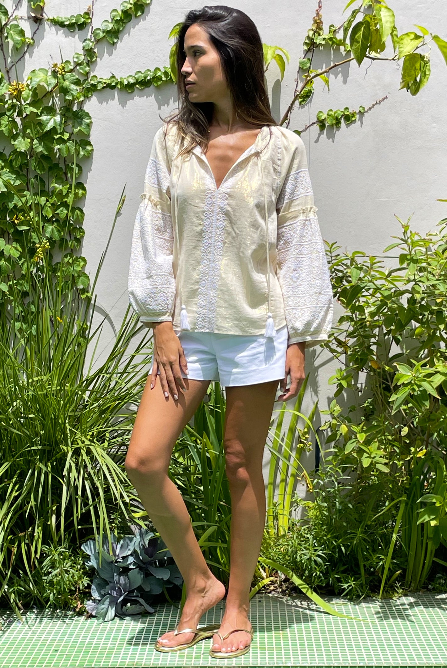 A model in a garden wearing the Rose and Rose gold lurex Capri embroidered top.
