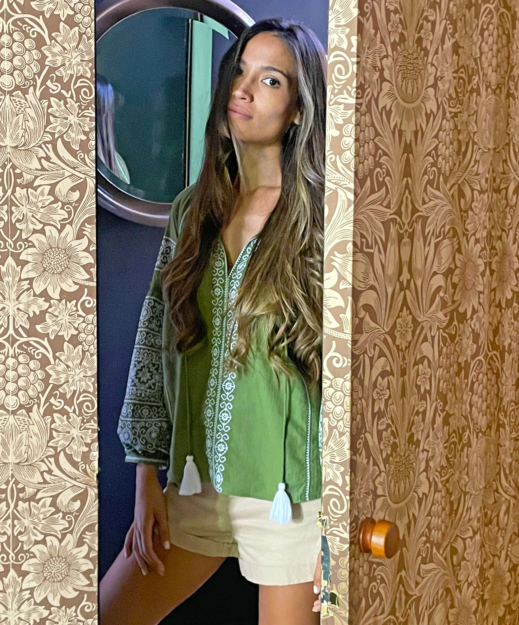 A model opening a door wearing the Rose and Rose Capri embroidered top in olive cotton.