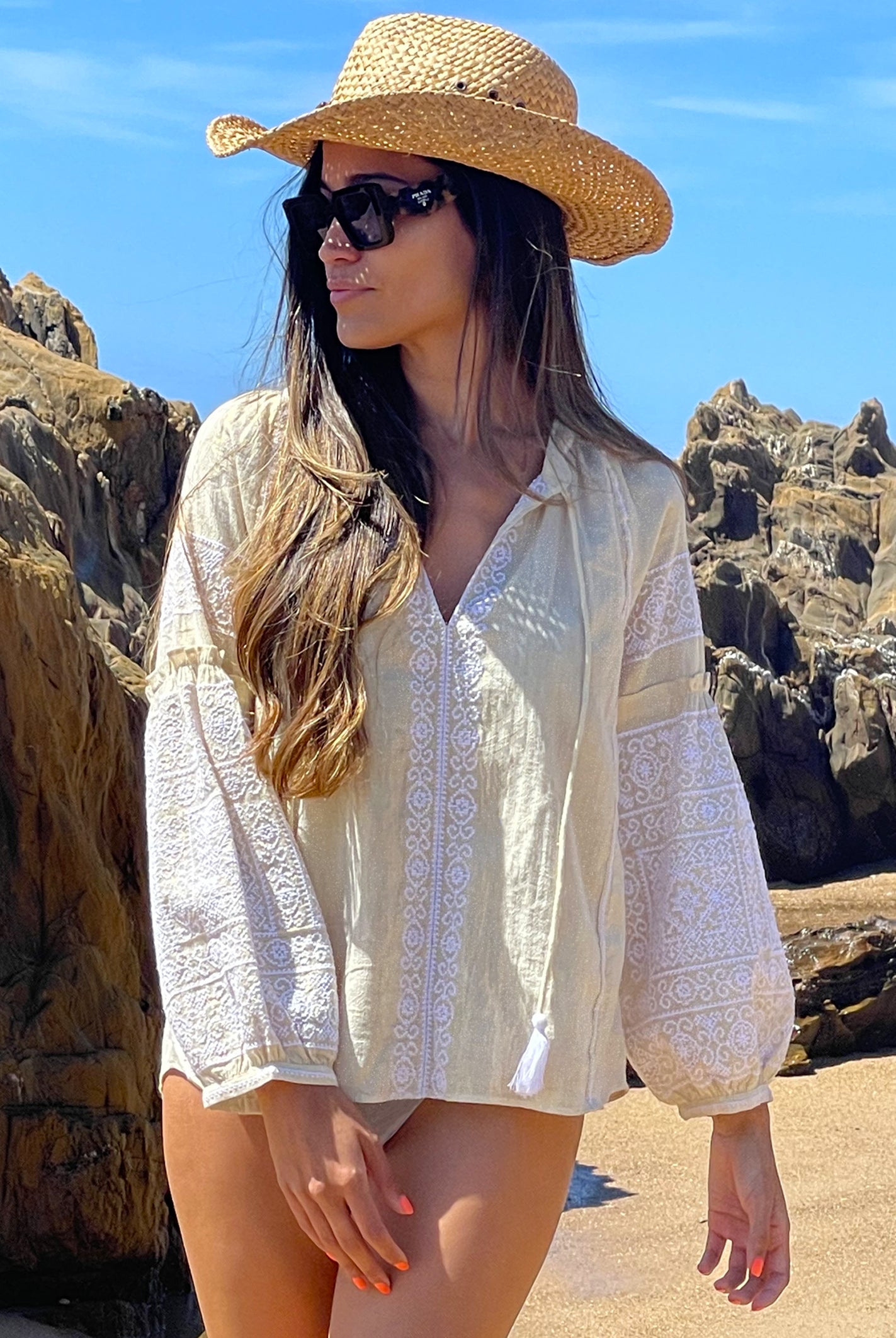 A model on a beach wearing the Rose and Rose gold lurex Capri embroidered top, straw cowboy hat and sunglasses.