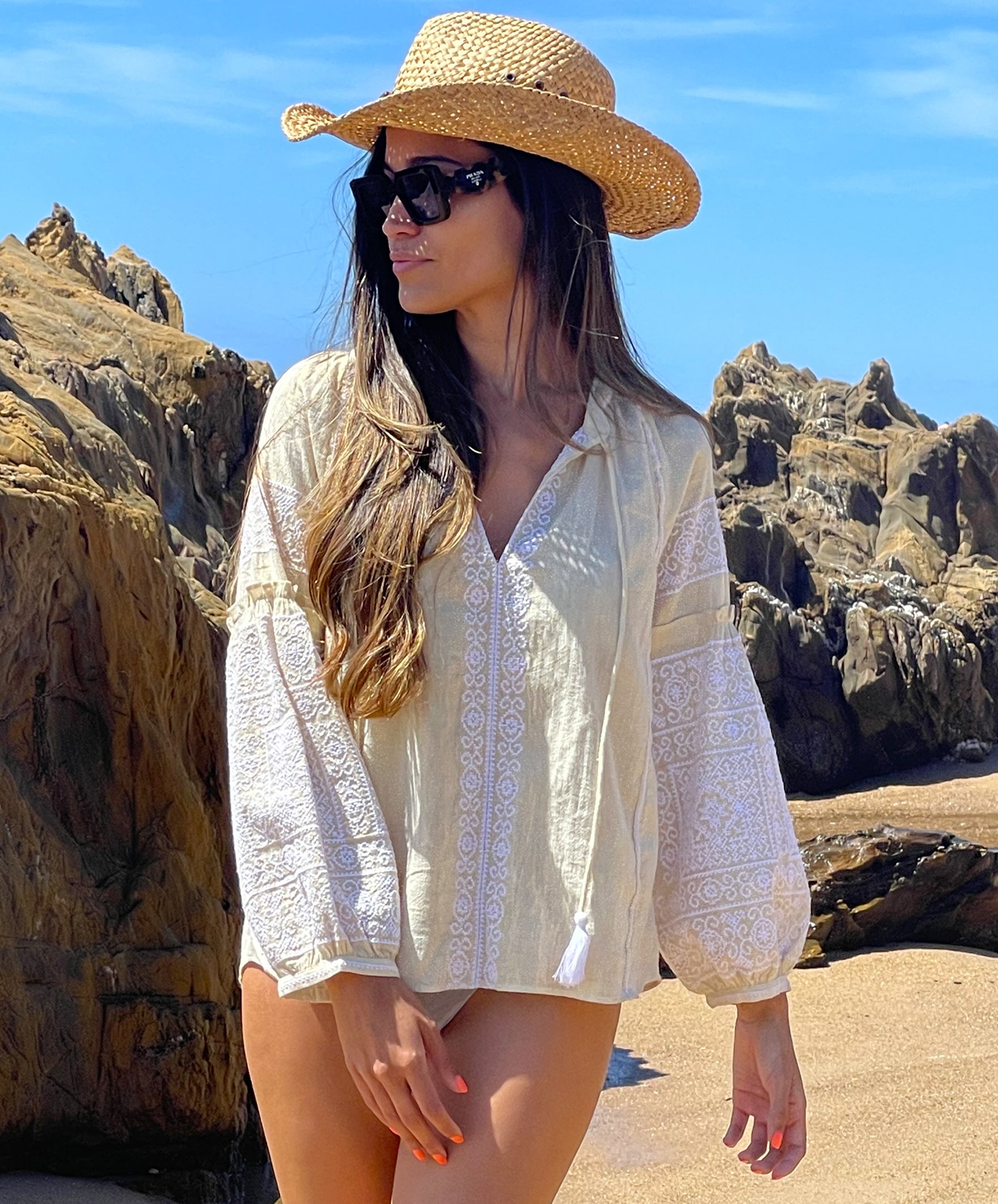 A model on a beach wearing the Rose and Rose gold lurex Capri embroidered top, straw cowboy hat and sunglasses.