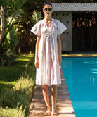 Woman in a light pink Carnation dress standing by a pool with greenery around
