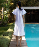 Back view of a woman in a white Carnation dress standing by a pool