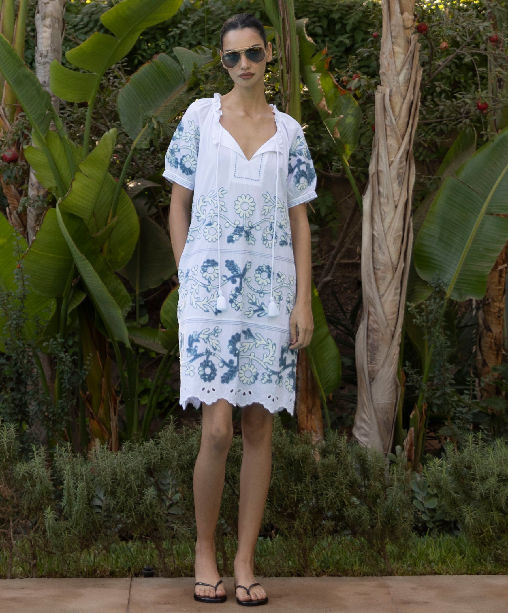 Model wearing aCedar white dress with blue denim applique decoration in a tropical garden setting