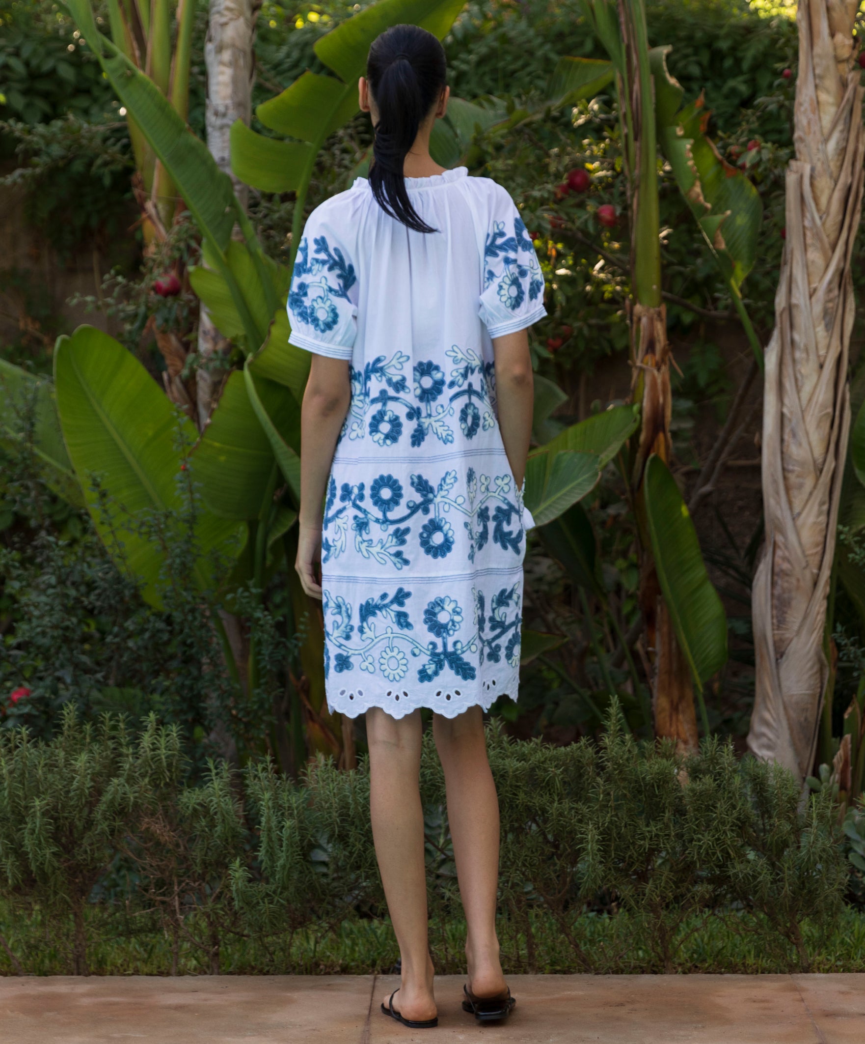 Back view of a model wearing a Cedar white dress with blue denim applique decoration.