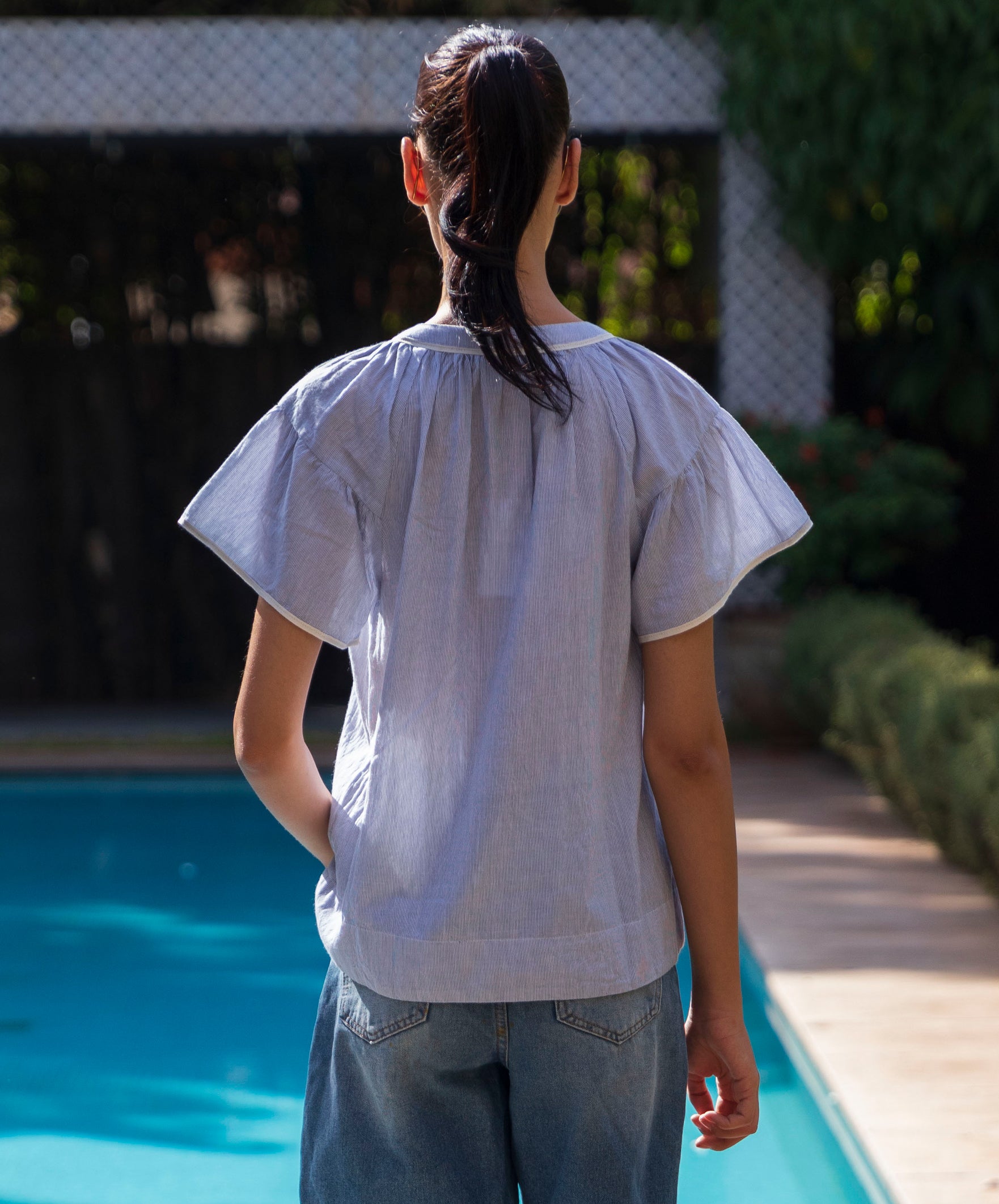 Back view of a woman wearing a blue striped Clematis top by a poolside