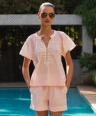 Woman wearing a pale pink Clematis blouse with matching shorts and sunglasses by a pool