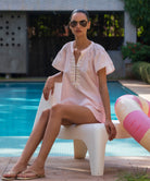 Woman in a light pink clematis blouse and matching shorts sitting by a pool with sunglasses on
