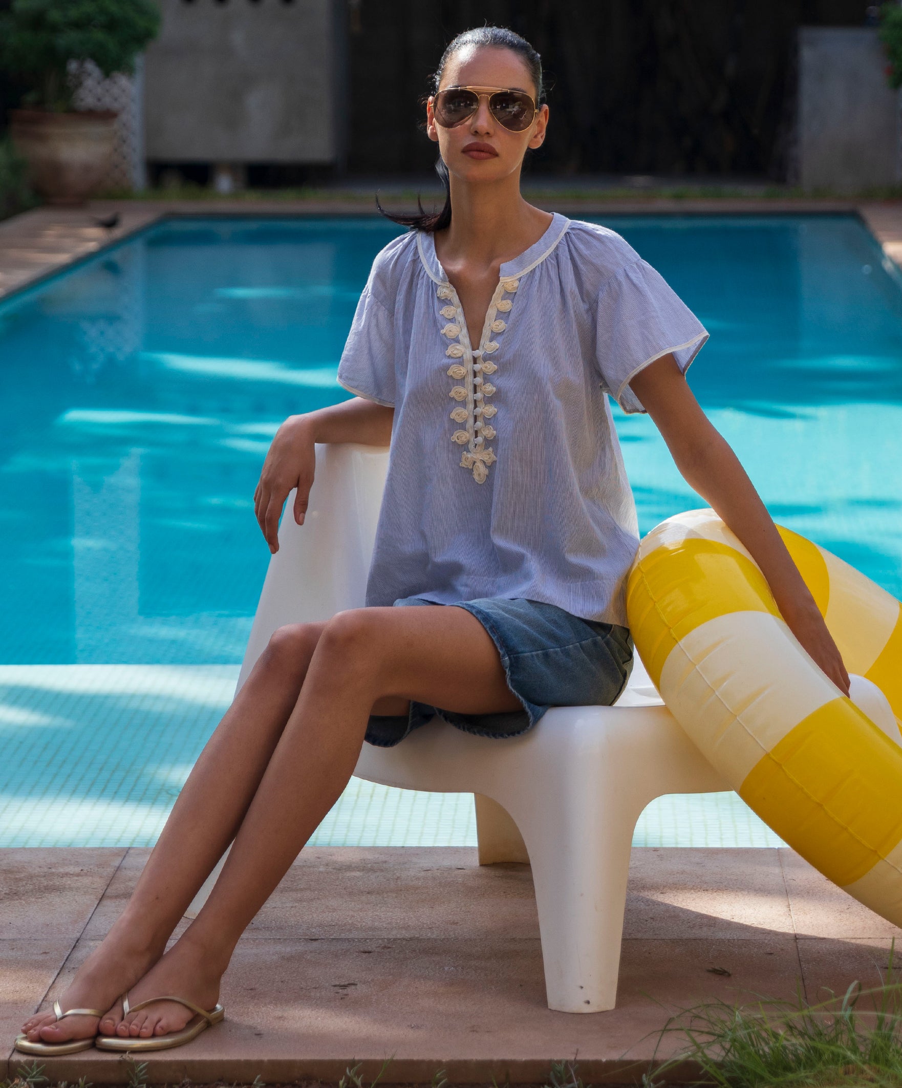 Woman sitting by a pool in a striped Clematis top with a yellow and white inflatable ring